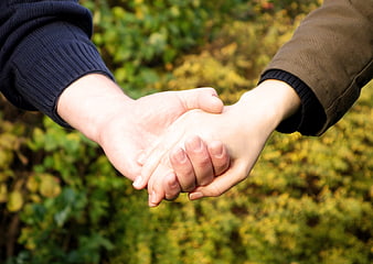 Close-up of two people holding hands outdoors in autumn