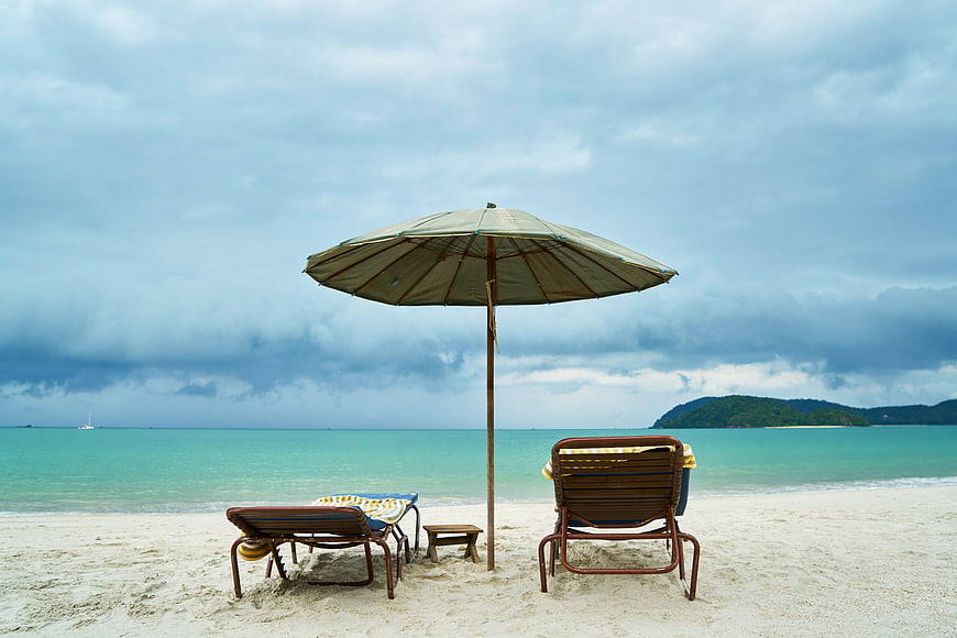 Tropical Beach Scene With Umbrella And Chairs Under Dramatic Sky