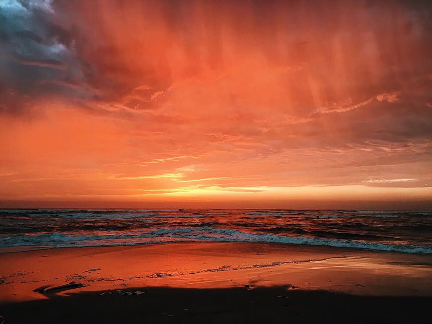 Dramatic fiery orange sunset over ocean waves and wet sandy beach