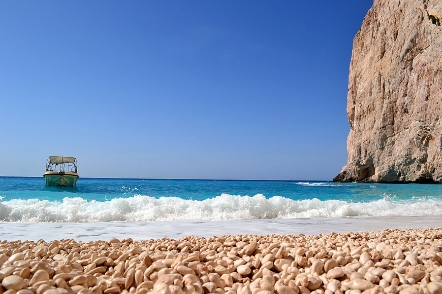 Turquoise Sea Waves Crashing on Pebble Beach with Boat