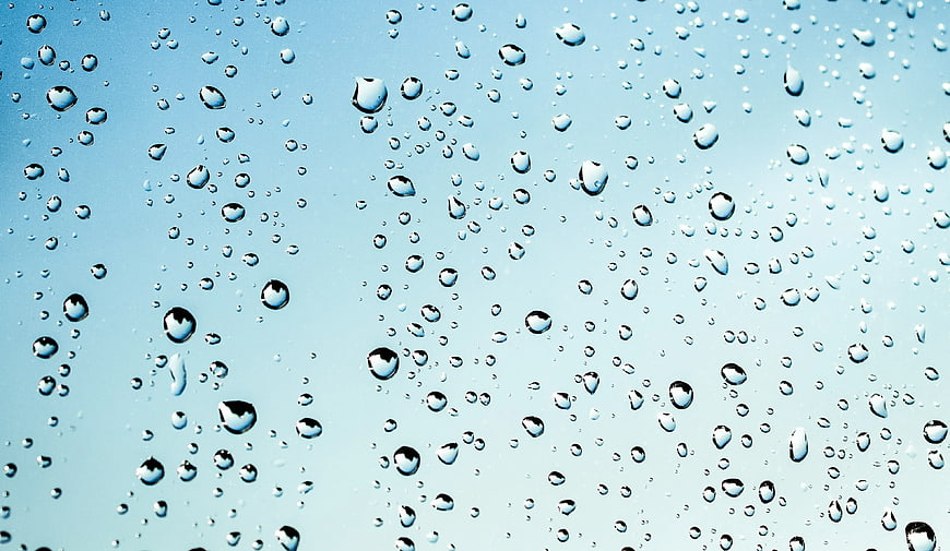 Water droplets on glass against blue sky background