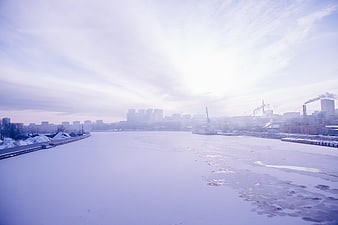 Frozen river landscape with distant industrial city skyline and smokestacks