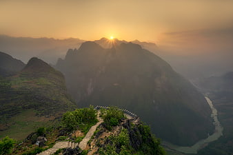 Sunrise over misty mountains with winding path and river