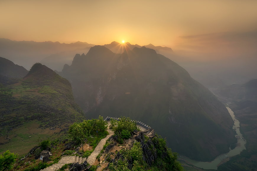 Sunrise over misty mountains with winding path and river