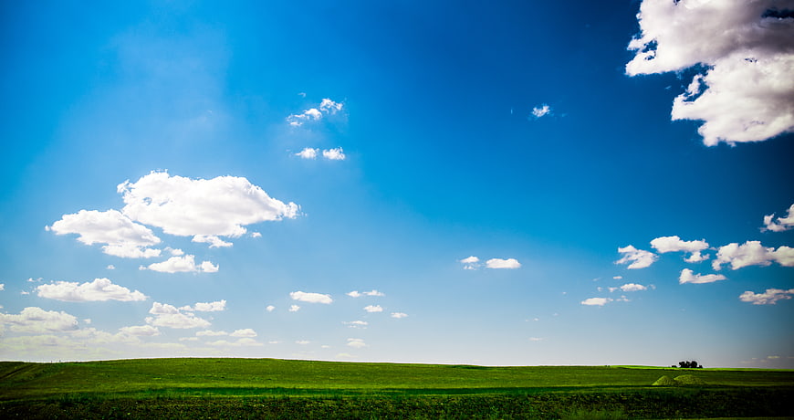 Vibrant Green Rolling Hills Under Blue Sky with Clouds