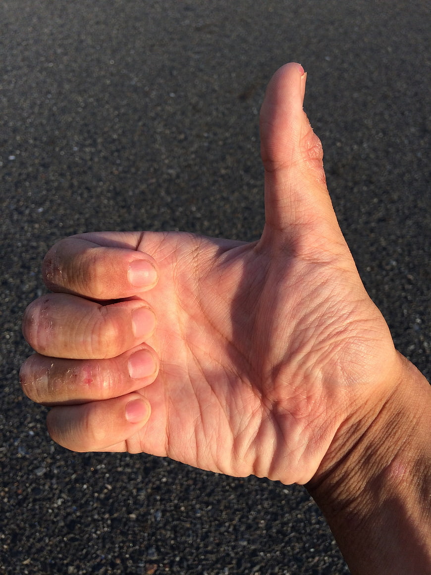 Close-up of hand giving thumbs up gesture on asphalt