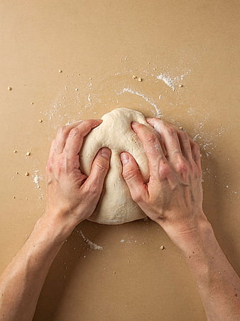 Hands kneading fresh dough on brown paper background