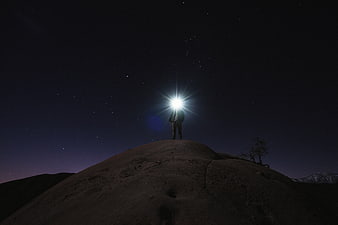 Silhouette of Person with Flashlight on Hill Under Starry Night Sky