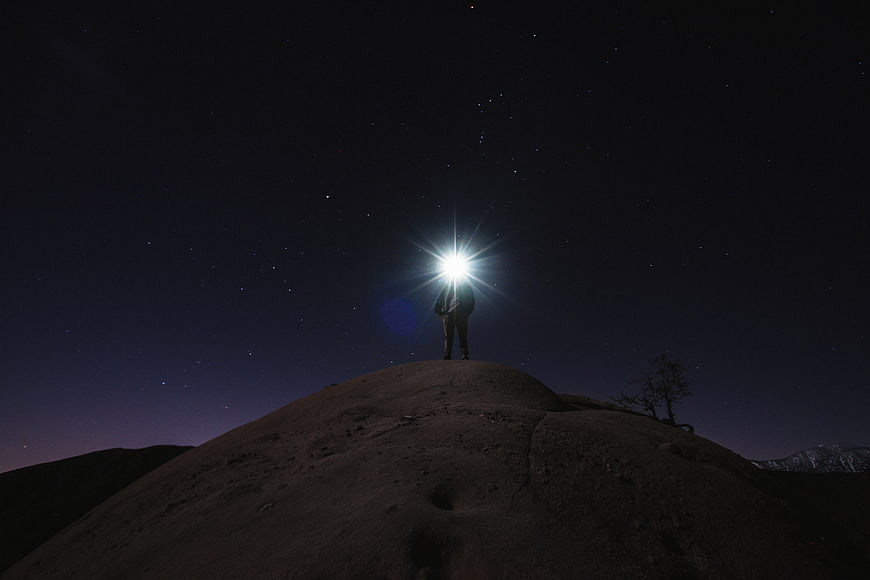Silhouette of Person with Flashlight on Hill Under Starry Night Sky
