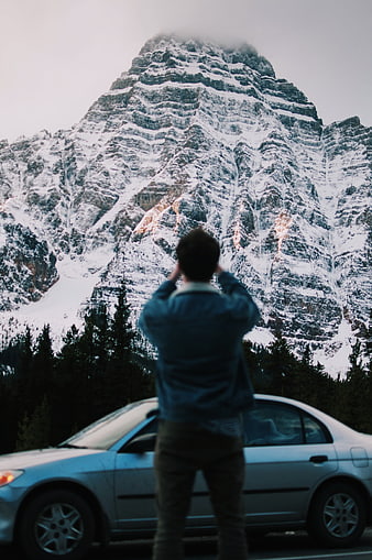 Man photographing snowy mountain peak from roadside