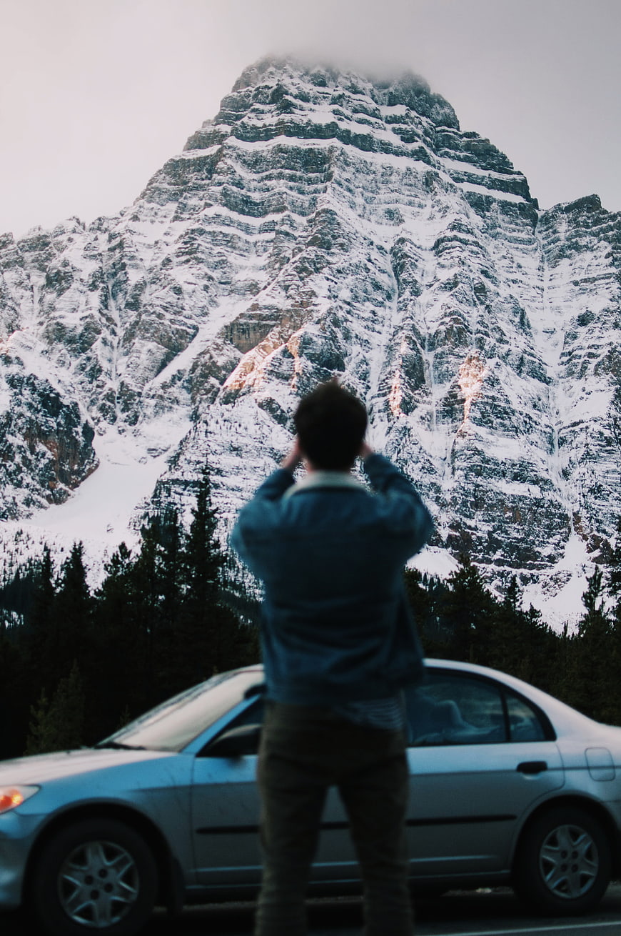 Man photographing snowy mountain peak from roadside