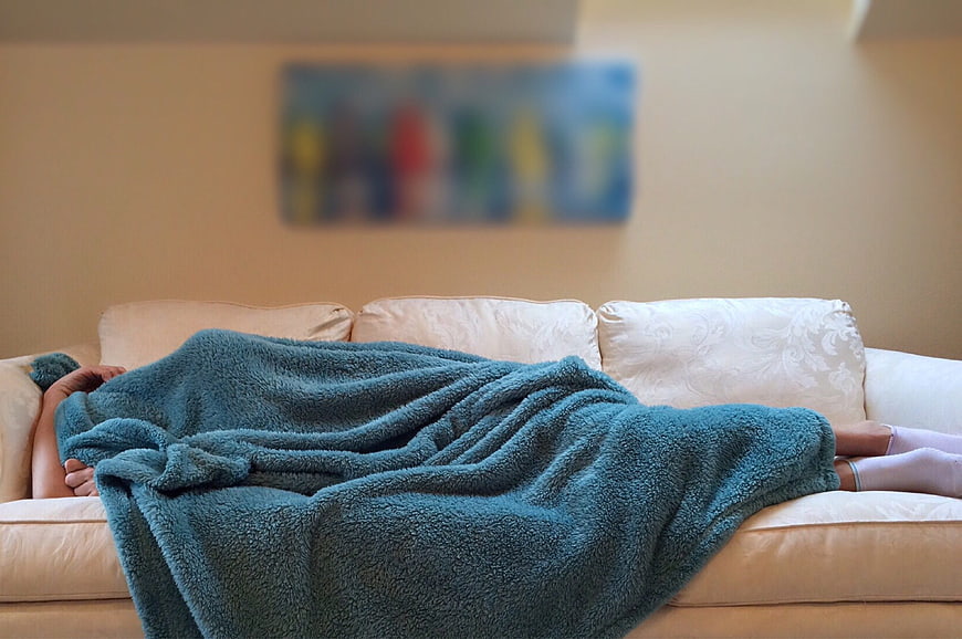 Person Sleeping Under Blue Blanket on White Sofa