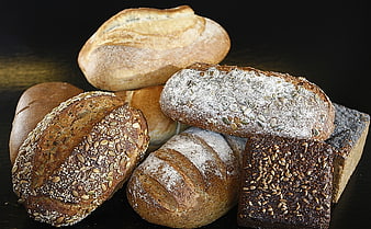 Assorted artisanal bread loaves with seeds and flour on dark background