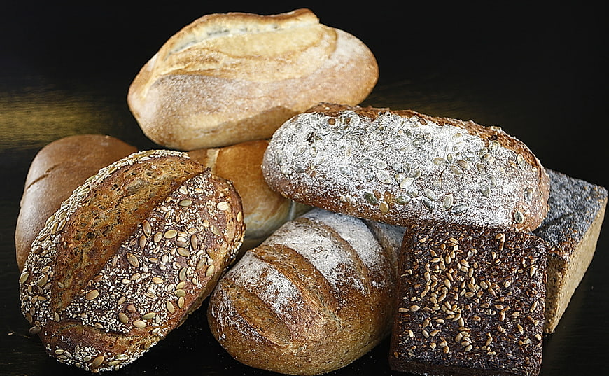 Assorted artisanal bread loaves with seeds and flour on dark background