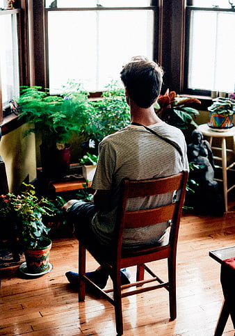 Man sitting on wooden chair looking at houseplants by window
