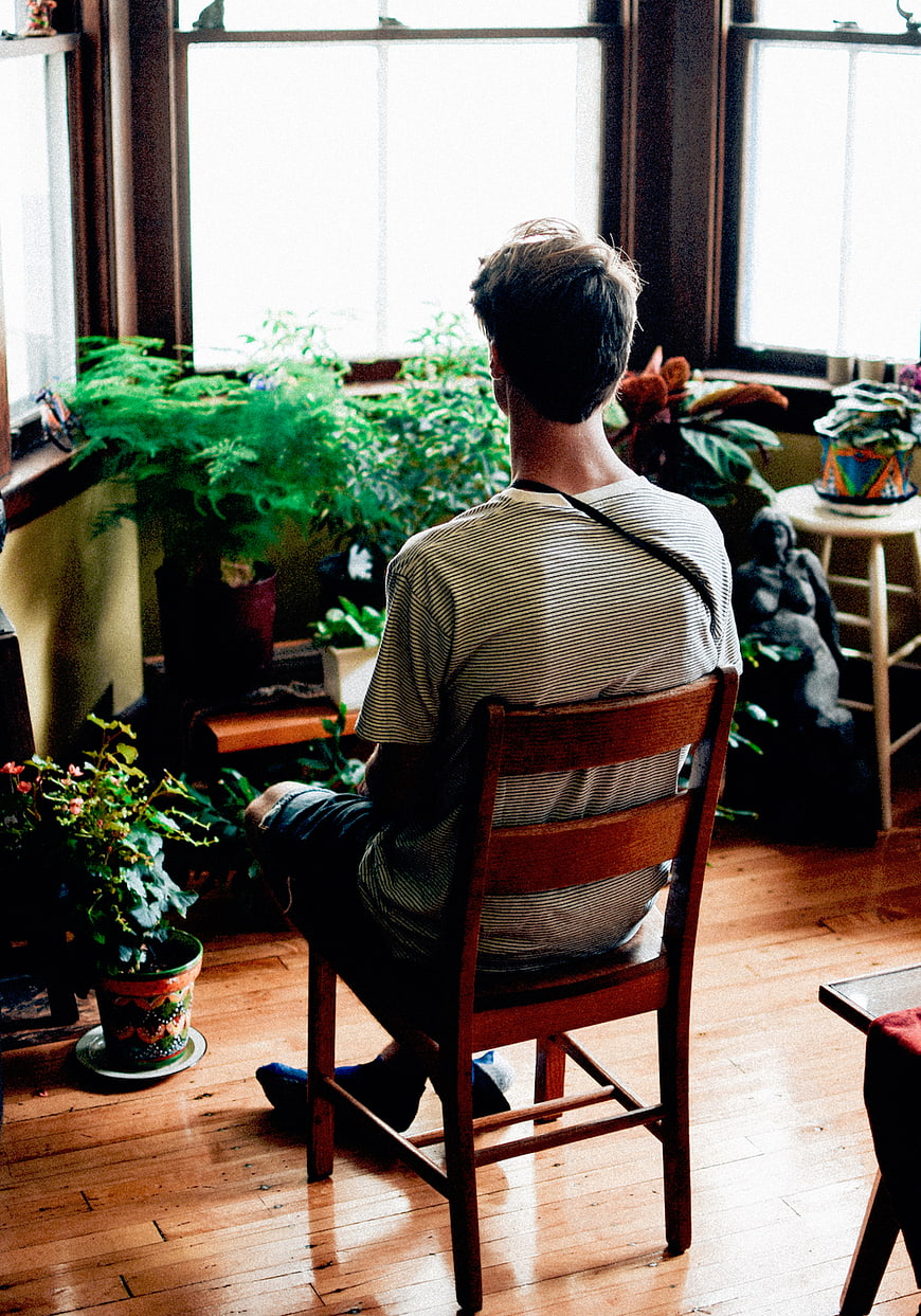 Man sitting on wooden chair looking at houseplants by window