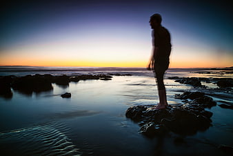 Silhouette of Man Standing on Rock at Sunset