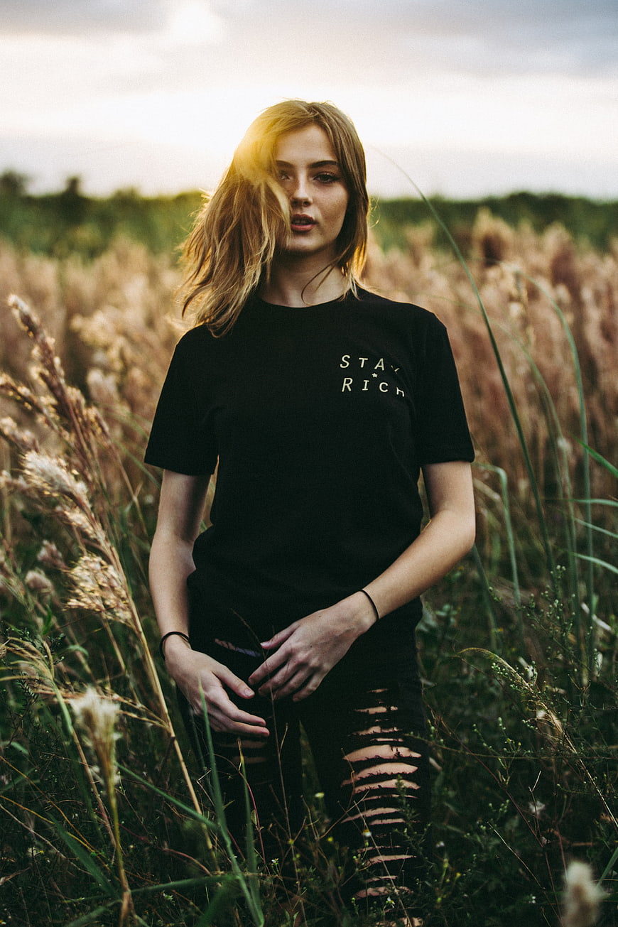 Blonde woman in black t-shirt standing in tall grass field
