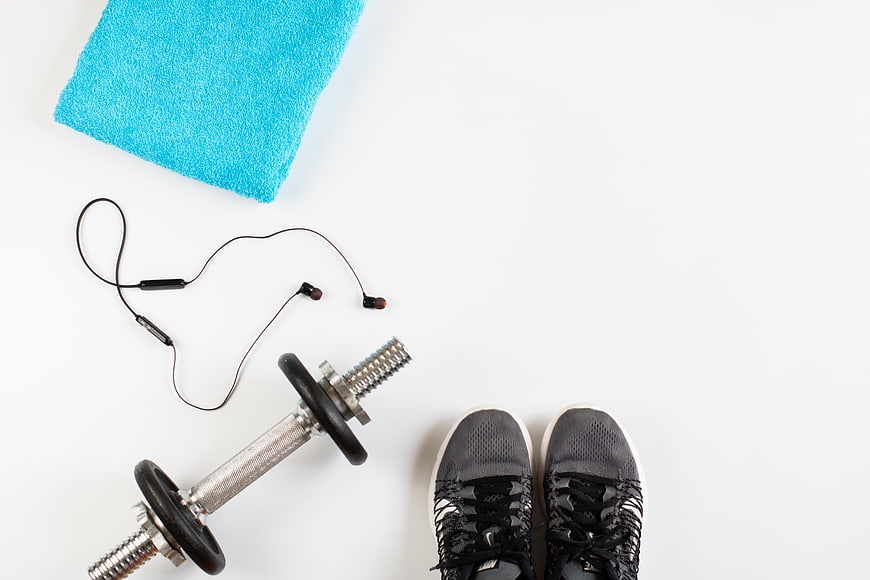 Flat lay of fitness gear with sneakers, dumbbell, and blue towel