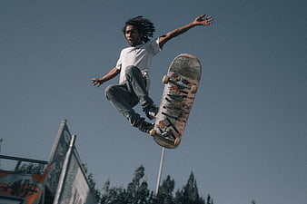 Skateboarder performing high jump trick against blue sky