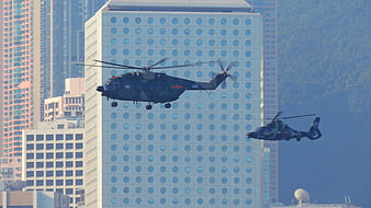 Two Military Helicopters Flying Past Modern High-Rise Building