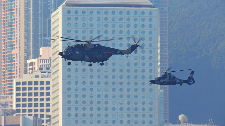 Two Military Helicopters Flying Past Modern High-Rise Building