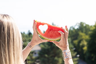 Woman holding watermelon slice with heart cutout outdoors