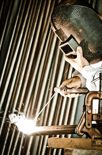 Welder in Helmet Creating Sparks on Metal Pipe