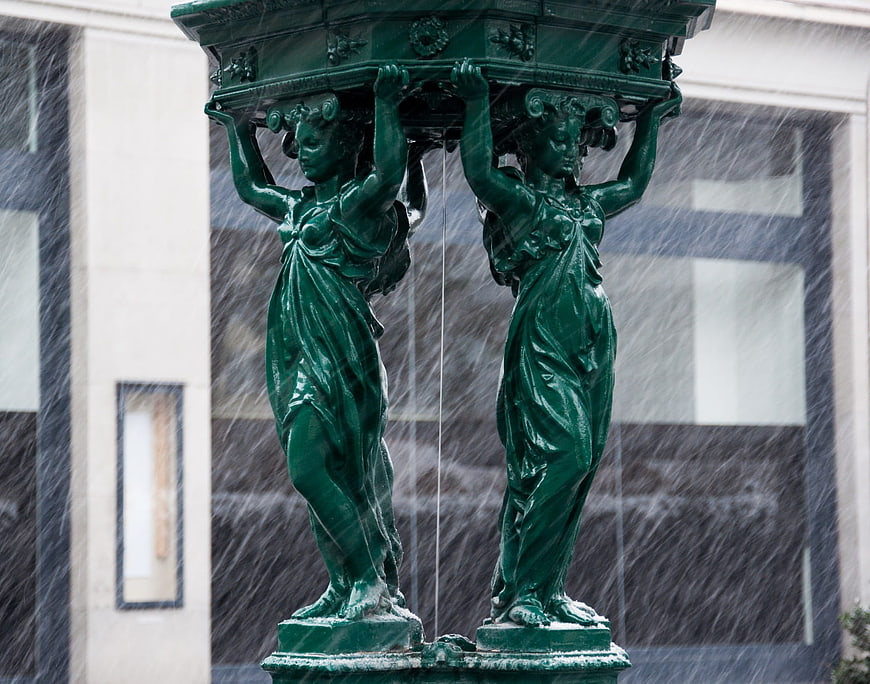 Green bronze caryatid fountain statues in heavy snowfall