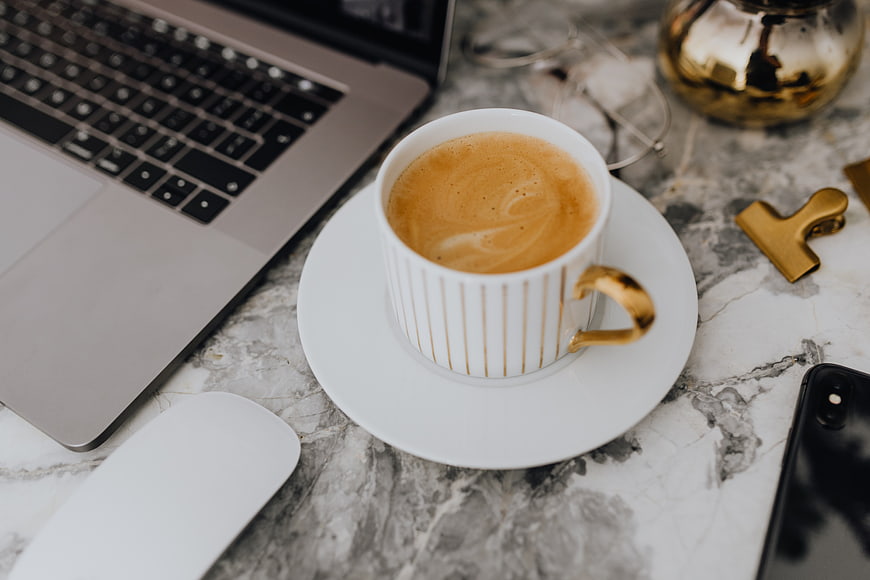 Flat lay of coffee cup, laptop, and office accessories on marble desk