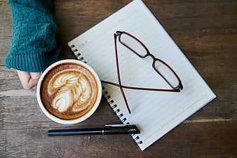 Flat lay of latte art, notebook, and glasses on wooden table