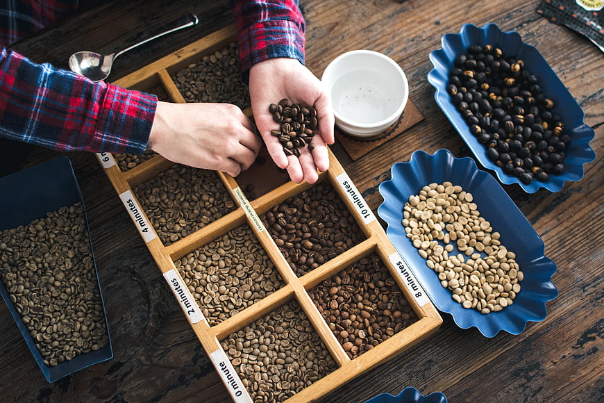 Top view of hands sorting roasted coffee beans on wooden tray