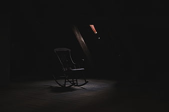 Lonely rocking chair in dark attic with shaft of light