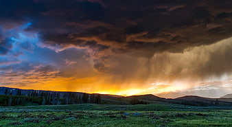 Dramatic Storm Clouds with Lightning Over Mountain Meadow at Sunset