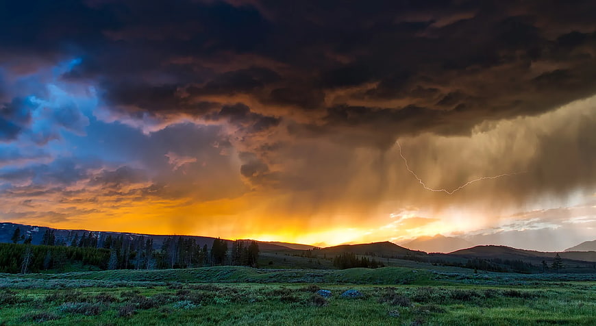 Dramatic Storm Clouds with Lightning Over Mountain Meadow at Sunset