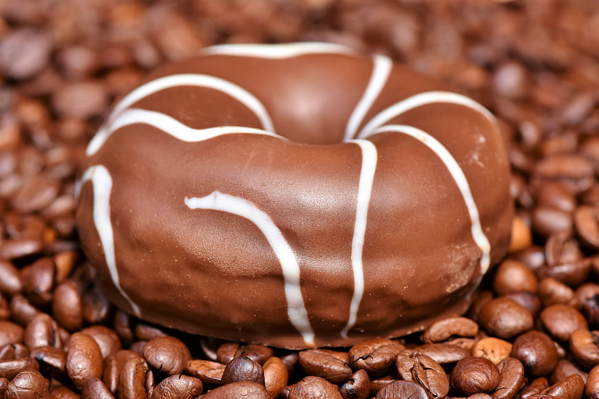 Chocolate glazed donut with white icing on coffee beans