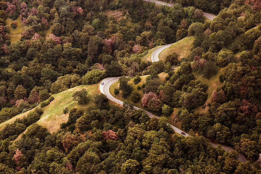 Aerial view of winding road through lush green forest hills