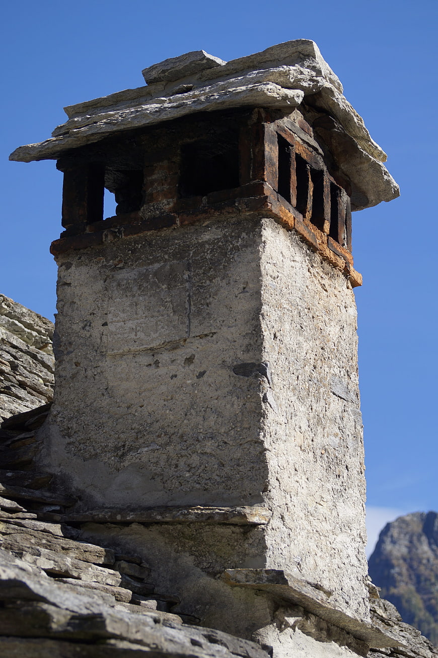 Rustic stone chimney on a traditional Swiss roof