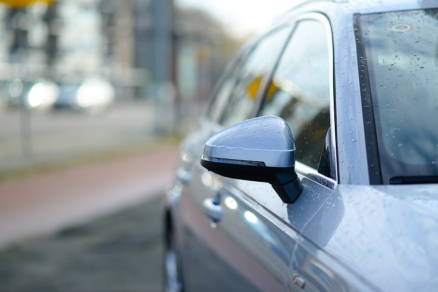 Close-up of silver car side mirror with raindrops