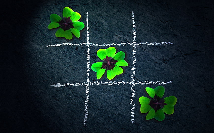 Four-leaf clovers winning a tic-tac-toe game on dark slate