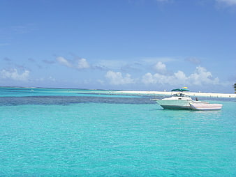 White boat anchored in turquoise tropical waters near white sandbar