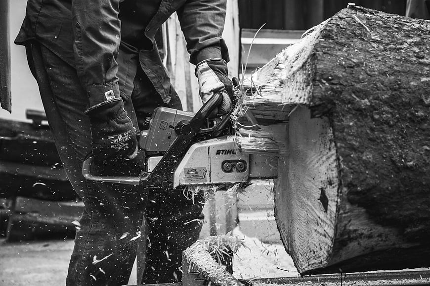Man Cutting Log with Chainsaw in Black and White