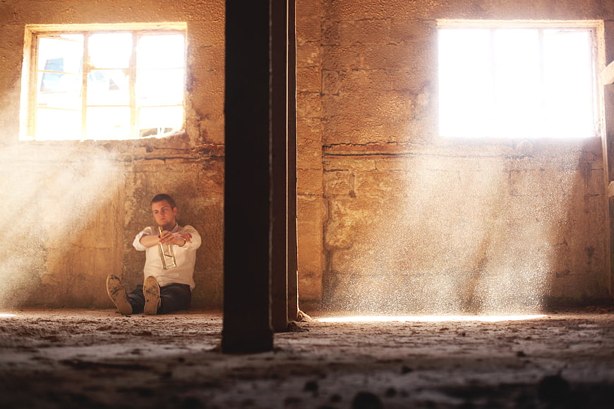 Man sitting with trumpet in dusty abandoned room with sunbeams