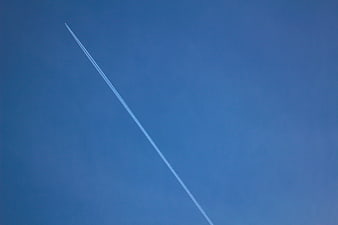 White airplane contrail streaking across clear blue sky