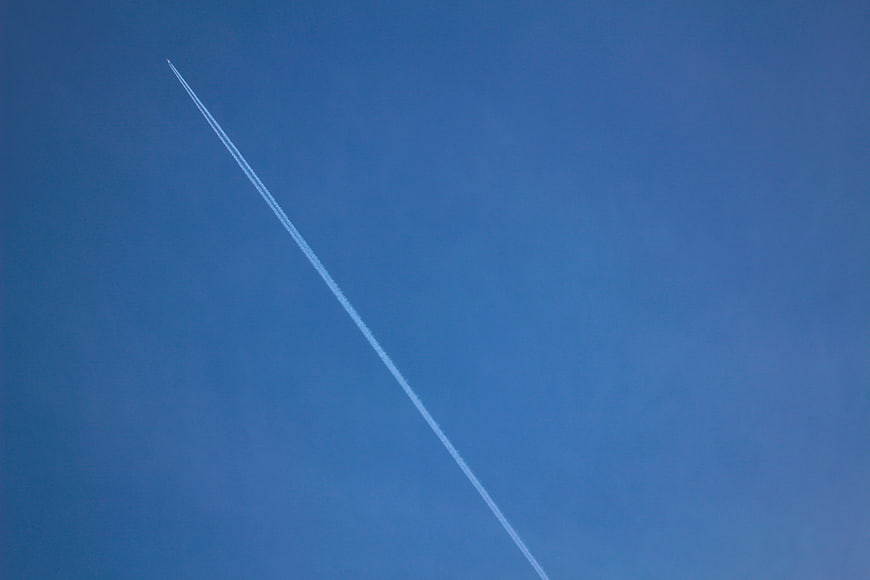 White airplane contrail streaking across clear blue sky