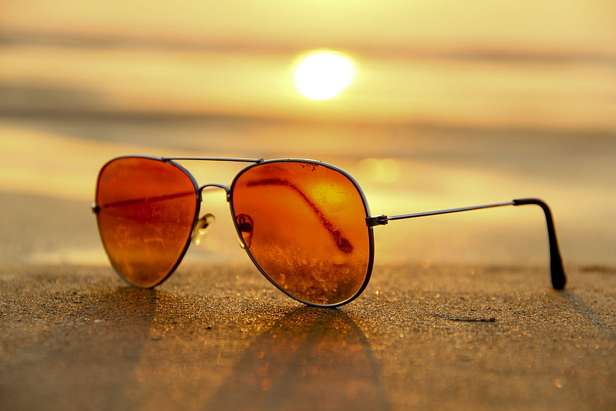 Aviator sunglasses with orange lenses resting on wet sand at sunset