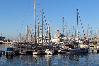 Sailboats docked in a busy harbor with large ship in background