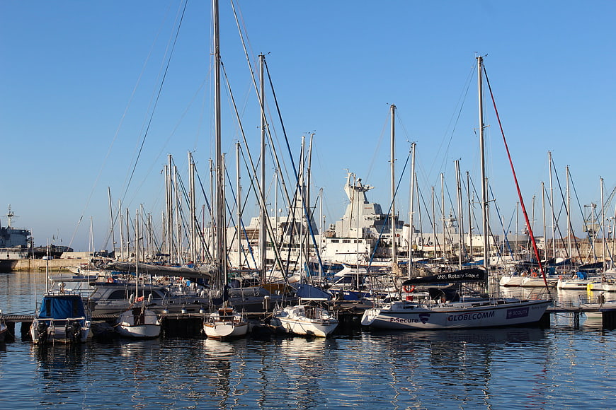Sailboats docked in a busy harbor with large ship in background