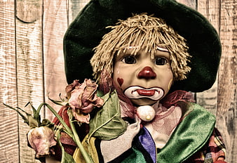 Sad vintage clown puppet holding dried roses against rustic wooden background