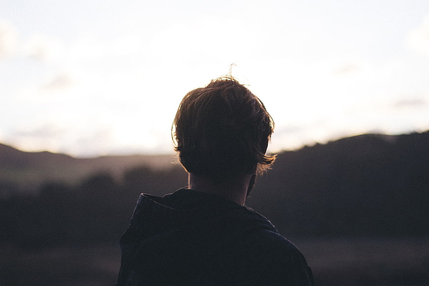 Silhouette of Man Looking at Sunset Over Hills
